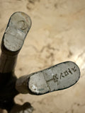 Close-up view of the underside of a vintage Popy 1975 Sofubi Kamen Rider Stronger figure’s feet. The left foot bears a molded stamp reading “X RAY” with an adjacent symbol, possibly a manufacturer’s mark. The right foot has a circular indentation, less legible but likely part of the original production mold. The surface is metallic and slightly worn, indicating age and authenticity.