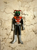 Upright front view of the Kamen Rider Stronger figure on a beige marbled surface. The figure wears a red chest plate with a black “S,” black limbs, silver gloves and boots, and a starburst belt. The helmet is green with red antennae, capturing the iconic tokusatsu hero look.