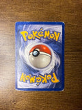 Pokémon card back on a wooden table, displaying Poké Ball design with mirrored yellow “Pokémon” text. Back angle 2.