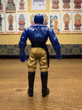 Back view of the Armored Captain Gatezone sofubi figure from Kamen Rider Black RX (1988). The figure wears a blue upper body suit with sculpted armor details, tan pants, and black boots. A black belt with a holster or strap hangs from the right side. The head is blue and helmeted, with arms positioned downward. The paintwork and sculpting reflect classic Showa-era craftsmanship, emphasizing its collectible value.