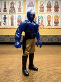 Side profile of the Armored Captain Gatezone sofubi figure from Kamen Rider Black RX (1988). The figure features a blue sculpted torso with armor-like ridges, beige pants, and black boots. The helmeted head includes a red circular detail, suggesting a robotic or villainous theme. A black belt with a holster hangs from the right side. The stylized proportions and paint application reflect the gritty aesthetic of late-80s tokusatsu design.