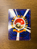 Back side of a Japanese Pokémon trading card placed on a wooden surface, showing a central Poké Ball with radiating white beams on a blue background. Yellow curved text reads “POCKET MONSTERS,” with a yellow ribbon labeled “CARD GAME.” Includes 1996 copyright information.