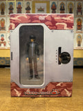 Military-themed DVD box set for 'Full Metal Panic!' featuring a central window that displays artwork of a mecha robot. The packaging includes green camouflage accents on the top and bottom edges and a metallic frame around the artwork. The top of the box reads 'DVD VIDEO' and the bottom features a metallic plate engraved with the title 'FULL METAL PANIC.' In the background, a wall is decorated with a grid of religious or spiritual images, possibly Buddhist deities, adding a contrasting cultural layer to the