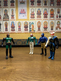 Four vintage Japanese tokusatsu action figures standing upright on a flat surface. The leftmost figure is Naval Commander Bosgun from Kamen Rider Black RX (1988), featuring a green and black armored suit with red compound eyes and insect-like antennae. The three figures to the right are stylized villains or allies from the same series, each with unique costumes: one in green and white with a red-and-white mask, one in blue with tan pants and a blue mask, and one in black and blue with a white animal-like he