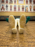 Close-up view of the underside of the Naval Commander Bosgun sofubi figure from Kamen Rider Black RX (1988), showing molded text and patterns on the soles of the shoes. The left sole is marked “CHINA” with additional faint characters, while the right sole has less legible molded details. The figure has green hands and off-white legs and shoes, confirming its soft vinyl construction and manufacturing origin—useful for authenticity verification and collector cataloging.