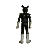 Full back view of the Kamen Rider Stronger figure standing upright. The figure wears a black suit with white gloves and boots, and a helmet featuring two red horn-like antennae. The belt and shoulder details are clearly visible, and the figure stands on a marbled beige surface with dark veining.