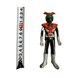 Front-facing view of the Kamen Rider Stronger figure standing beside a measuring tape showing a height of approximately 10.1 cm. The figure wears a red and black suit with silver gloves and boots, green compound eyes, and a red helmet crest. A bold black “S” emblem is centered on the chest, and a starburst design decorates the belt.