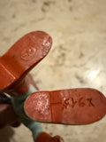 Close-up of the underside of the figure’s feet. The left foot has an oval emblem with the letter “R” molded inside. The right foot is engraved with “X945,” likely a production or mold code. The figure is held in hand, showing painted plastic with wear consistent with vintage age.