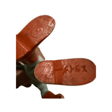 Close-up view of the underside of a vintage Popy Sofubi Kamen Rider X figure’s feet. The left foot has an oval-shaped molded mark with the letters “F P” embossed inside, indicating the manufacturer. The right foot features an engraved alphanumeric code “494X,” likely a mold or production identifier. The figure is painted red and blue, and the plastic shows signs of age.