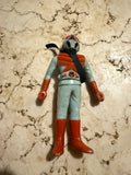 Overhead view of the Kamen Rider X figure lying flat on a marbled surface. The figure wears a light blue suit with red chest armor, gloves, and boots. The helmet is gray with red accents and a black visor, and a black ribbon or strap wraps around the neck. The figure shows signs of age, consistent with vintage sofubi toys.