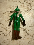 Vintage Kamen Rider Amazon sofubi figure lying face down on a marbled surface. The figure wears a green outfit with brown boots and black gloves, a white scarf, and a pointed helmet. Visible wear and scuff marks suggest age and use, adding character for collectors interested in condition grading and authenticity.