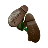 Close-up of the underside of a vintage sofubi figure’s feet, showing embossed Japanese text. The left foot reads “マグマ” (Maguma), possibly referencing a character or variant name. The right foot features an oval stamp with Japanese text and the year “1982 JAPAN,” confirming the figure’s origin and production date. The feet are molded in dark brown vinyl, consistent with the rare limb color variant of Kamen Rider Amazon.