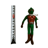Front-facing view of the Kamen Rider Amazon sofubi figure standing beside a vertical measuring tape, indicating a height of approximately 10 cm. The figure has a green body, red chest armor, dark brown gloves and boots, and a white scarf. The helmet features red compound eyes and an insect-like crest, confirming its identity as the Amazon Rider. This image provides scale reference for collectors.