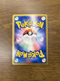 Back side of an official Pokémon trading card placed on a wooden surface, featuring a central Poké Ball with a multicolored glow, surrounded by six elemental energy symbols. The card displays the yellow “POKÉMON” logo at the top and bottom on a blue gradient background with a yellow border.