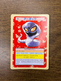Back side of a vintage Japanese TopSun Pokémon card placed on a wooden surface, featuring a diagonal green text pattern that reads “ポケモンカード” (Pokémon Card) and “トップサン” (TopSun)
