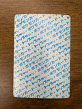 Back side of a Japanese TopSun Pokémon card placed on a wooden surface, showing a white background with repeating blue Japanese text “ポケモンカード・トップサン,” indicating it is part of the vintage TopSun series.