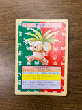 Japanese TopSun Pokémon card featuring Exeggutor (ナッシー) placed on a wooden surface, with a vibrant green and red background and silhouettes of other Pokémon. Includes Japanese text with Grass and Psychic types, height, weight, and signature moves.