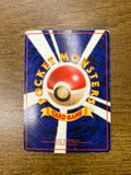  Back side of a Japanese Pokémon trading card placed on a wooden surface, showing a central Poké Ball with radiating white beams on a blue background. Yellow curved text reads “POCKET MONSTERS,” with a yellow ribbon labeled “CARD GAME.” Includes 1996 copyright information.