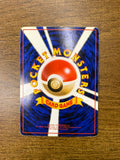 Back side of a Japanese Pokémon trading card placed on a wooden surface, showing a central Poké Ball with radiating white beams on a blue background. Yellow curved text reads “POCKET MONSTERS,” with a yellow ribbon labeled “CARD GAME.” Includes 1996 copyright information.
