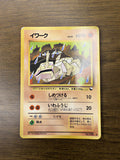 Japanese Onix (イワーク) Pokémon card placed on a wooden surface, showing Onix in a stylized pose with water droplets and rocky terrain. Features 70 HP, Level 25, two attacks—“しめつける” and “いわふうじ”—Grass weakness, and card number No.095. Illustrated by Tomokazu Komiya.