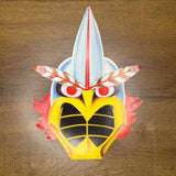Stylized cardboard mask of a bird-like creature with yellow beak, red eyes, blue crest, and red wing-like sides.