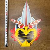 Colorful bird mask placed on a wooden surface, featuring bold colors and a measuring tape showing 30 cm height.