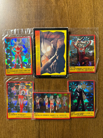 Collection of six Ultraman-themed trading cards arranged on a wooden surface. Five cards have holographic designs with red borders and Chinese text boxes, featuring characters like Father of Ultra, Mother of Ultra, Zoffy, and a group of eight Ultramen. The central card is non-holographic with a close-up of an Ultraman character and 'ULTRAMAN' printed in red."