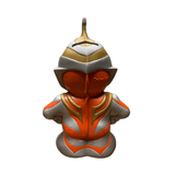 Close-up front view of the Ultraman Gaia piggy bank, showcasing a futuristic helmet with a pointed crest and smooth, featureless face. The figure is painted in orange, gold, and silver tones, with the embossed text “Daiwa Bank” prominently displayed on the chest. This indicates the item may have been a promotional tie-in or branded collectible, merging corporate sponsorship with pop culture appeal.