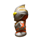 Side view of the Ultraman Gaia piggy bank, featuring a metallic silver body with red and gold accents and a large yellow eye. The figure has a cartoonish, oversized head and compact body. Embossed text “Coin Bank” is visible on the side, confirming its dual function as a savings container and collectible figure. The design blends utility with pop culture styling.