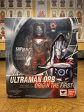 Boxed Ultraman Orb Origin The First S.H.Figuarts figure placed in front of a wall with religious artwork. The packaging displays the figure through a clear window and includes branding, Japanese text, and Tamashii Nations logo.