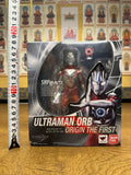 Boxed Ultraman Orb Origin The First S.H.Figuarts figure placed in front of a wall with religious artwork. The packaging displays the figure through a clear window and includes branding, Japanese text, and Tamashii Nations logo.