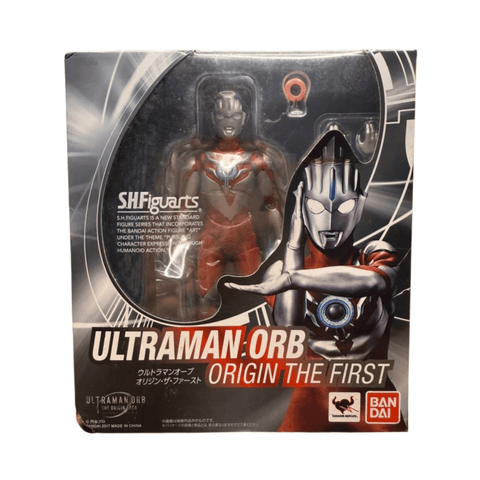 Close-up of Ultraman Orb Origin The First S.H.Figuarts box showing the figure in red and silver armor through a clear window. Includes branding, character name in English and Japanese, and dynamic illustration on the side.