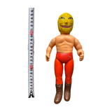 Upright view of the Golden Mask figure standing beside a vertical measuring tape, indicating a height of approximately 20 cm. The figure wears a yellow mask with fierce expression, red pants, and brown boots. The muscular build and dramatic mask design reflect the stylized villain aesthetic of 1970s Tiger Mask sofubi toys.