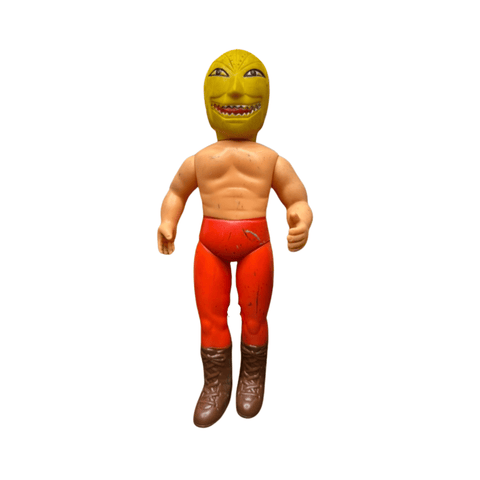 Detailed view of the Golden Mask figure’s upper body and head. The yellow mask has large eyes, sharp teeth, and a monstrous expression. The figure’s muscular torso is shirtless, and the red pants are sculpted with folds and creases. Brown boots and a belt complete the costume, emphasizing the wrestling villain persona.