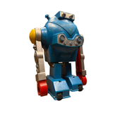 "Close-up of a vintage toy robot made of blue plastic with red and silver parts. One compartment is open, revealing internal wiring and a small motor. The toy includes gear-like structures, hinged sections, and wheels, suggesting mechanical functionality. Molded details simulate robotic features, highlighting mid-century toy engineering."