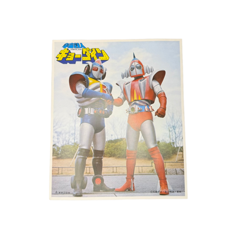 Two Kyōdain characters in retro robot costumes shake hands outdoors, wearing blue and red armor with helmets.