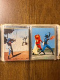 Open photo album page displaying four dramatic images of costumed characters from a Japanese fantasy or tokusatsu series. The top left shows a red-helmeted hero pointing forward. The top right depicts a confrontation between black and red-costumed characters. The bottom left features a character in a red cape and yellow pants in a dynamic pose. The bottom right shows a sun-faced villain in a golden robe holding a staff. Japanese text “日本テレビ・東宝” appears in one image, linking it to Nippon TV and Toho producti