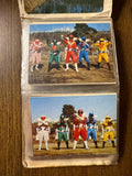 Two vintage collectible cards in a plastic sleeve. The top card shows a red-suited superhero riding a white motorcycle labeled “RED” and “GOR,” referencing Goranger. The bottom card features a yellow-suited hero in a dynamic pose with industrial structures in the background. These cards highlight individual team members from Himitsu Sentai Goranger, showcasing their vehicles and action stances.