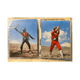 Two vintage Japanese superhero trading cards in a protective sleeve. The left card shows a dark-suited character with red chest armor holding a boomerang-like weapon, pointing forward. The right card features a red-suited hero aiming a weapon with both hands. Both cards are set against a natural outdoor backdrop with a mountain—possibly Mount Fuji—in the distance. The right card includes “©石森プロ NET 東映,” confirming its Goranger origin.