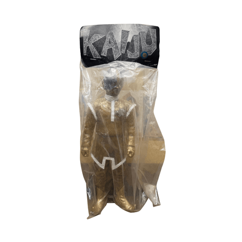 Full view of the Shapley Alien sofubi figure in sealed packaging. The header card features the word “KAIJU” in stylized, jagged font on a black and silver background. The figure is dressed in a metallic gold bodysuit with white trim, white boots, and a silver helmet with perforated detailing. The clear bag allows full visibility of the figure’s sculpt and paintwork, ideal for collectors.