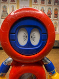 Detailed close-up of the Batten Robomaru GB-94 robot’s head, showing a red circular helmet and blue faceplate with two oval eyes featuring inward-pointing black arrow markings. The body is red with metallic silver joints and blue and yellow arms. The stylized eyes give the figure a distinctive and whimsical expression, emphasizing its cartoon-inspired design.