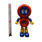 Full-body view of the Batten Robomaru GB-94 figure standing upright beside a vertical measuring tape, indicating a height of approximately 20 cm. The robot features a red circular head with blue cartoon-style eyes, a red torso with a transparent chest window, blue arms with yellow claw-like hands, and yellow legs with blue feet. The image provides a clear size reference for collectors and sellers.