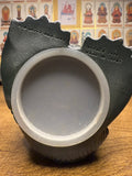 "Bottom view of a decorative item with a circular translucent base and jagged upper edge resembling a crown. Embossed text on the left reads '©TAKARA CO., LTD. 1995' and on the right 'TAKARA 1995 MADE IN JAPAN.' The item rests on a wooden surface, with a background wall featuring framed images of Buddhist deities labeled in Japanese."