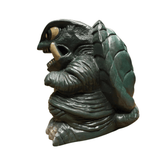 "Stylized turtle-like creature figurine with exaggerated features including bulging eyes, prominent tusks, and a wrinkled dark gray body. The segmented shell is dark green, and the overall color scheme blends green and gray tones. The design suggests a fantasy or sci-fi monster character with a mix of realism and cartoonish exaggeration."