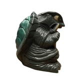 "Cartoonish turtle-like figurine with a large green segmented shell and a dark, wrinkled body. The creature has a prominent head with a large eye and a pointed beak-like mouth. It holds a small object in one hand, possibly a weapon or tool. The design is detailed and imaginative, suggesting a fantasy or pop culture inspiration."