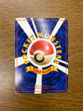 Back side of a Japanese Pokémon card placed on a wooden surface, showing a central Poké Ball with white beams on a blue background. Yellow curved text reads “POCKET MONSTERS,” with a yellow ribbon labeled “CARD GAME.” Includes 1996 copyright info.